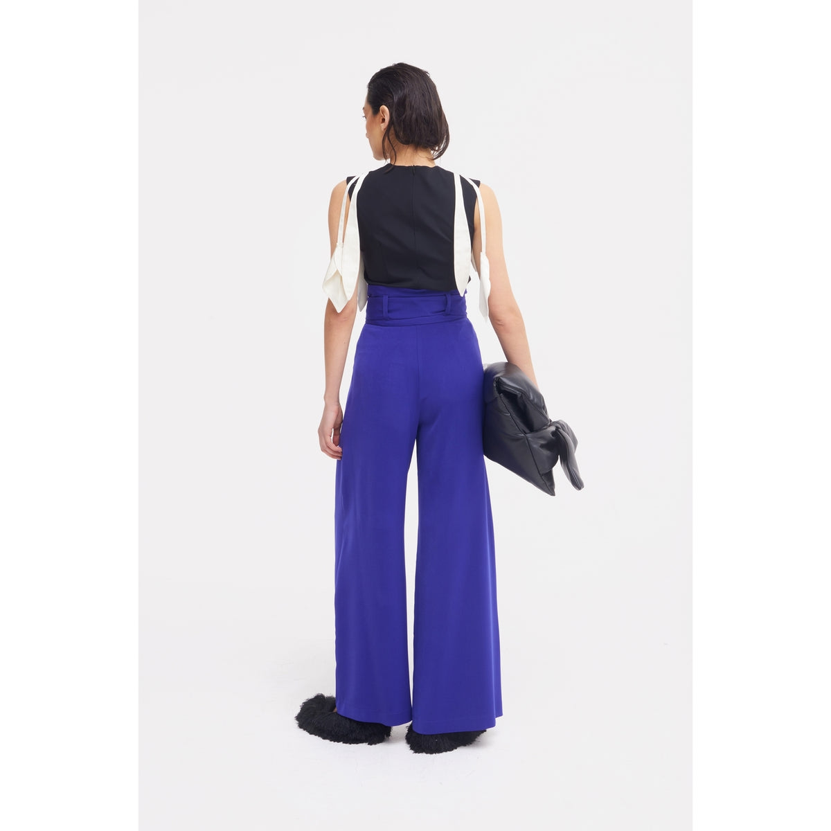 Someone stands facing away in a sleeveless black top with white accents, JULIA ALLERT Blue High Waist Long Wide Leg Trousers, black fuzzy shoes, and holding a black clutch against a plain white background.