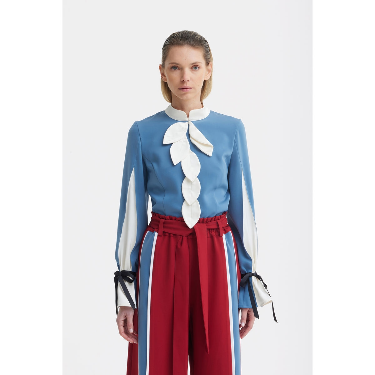 A woman faces forward, wearing a blue blouse with white leaf details and long sleeves, paired with JULIA ALLERT Belted High Waist Wide Leg Pants in burgundy featuring blue and white vertical stripes.