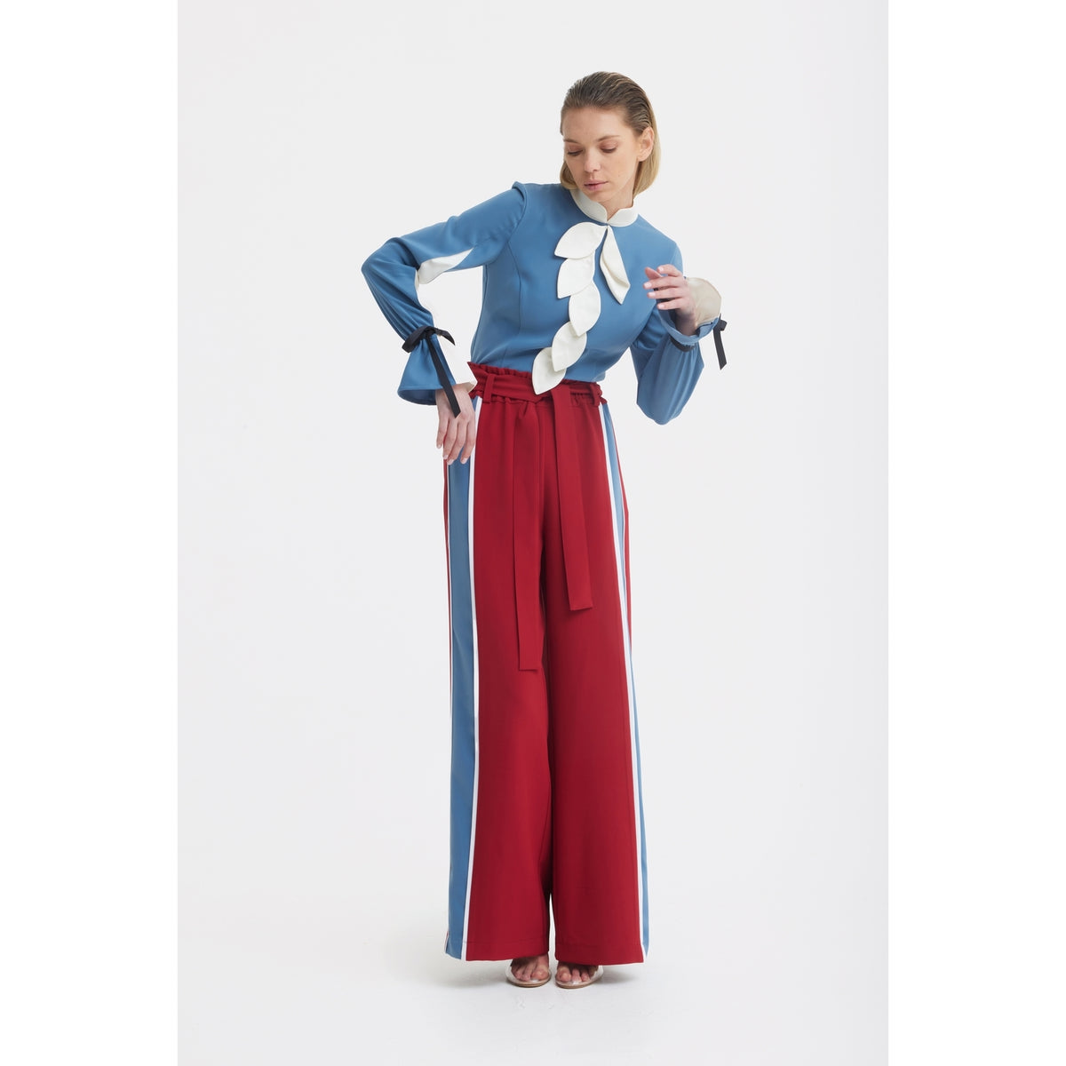 A woman poses against a white background wearing a blue long-sleeve top with white leaf details and JULIA ALLERT Belted High Waist Wide Leg Pants in burgundy, featuring a paperbag waist and blue-and-white side stripes.