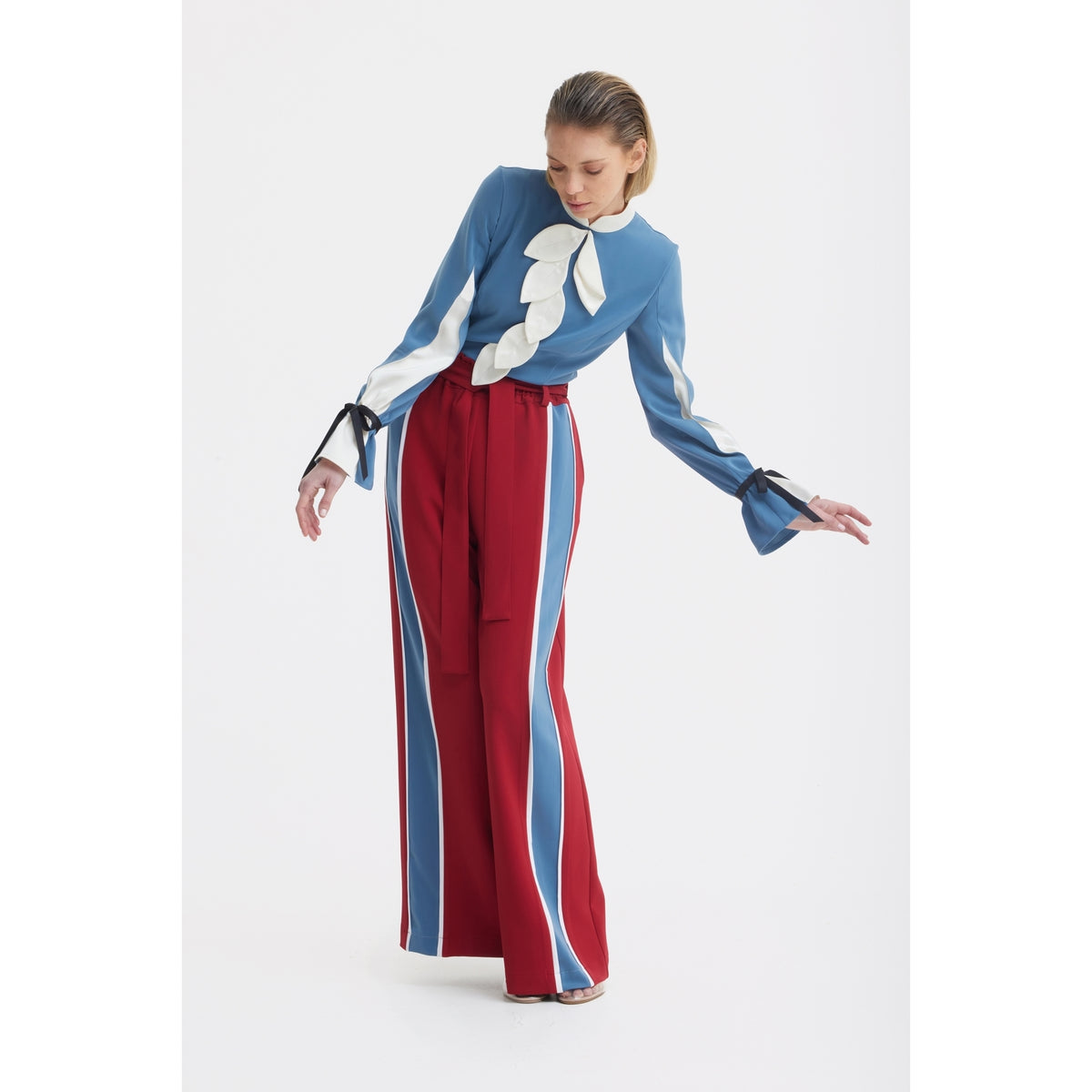 A person wears a blue blouse with white ruffles and JULIA ALLERT Burgundy Belted High Waist Wide Leg Pants, posing against a plain white background.