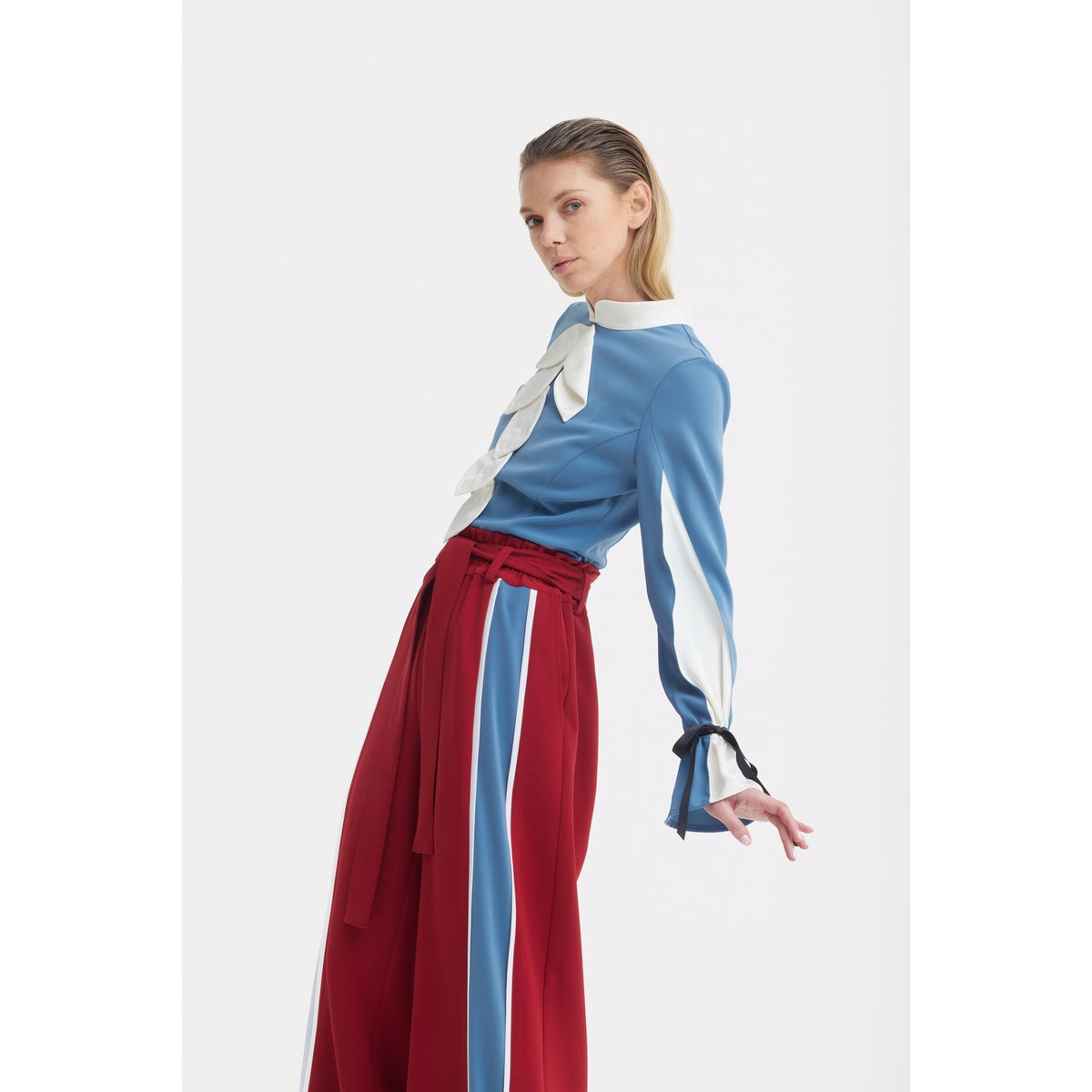 A woman poses against a white background, wearing a light blue blouse with white accents and a bow at the neck, paired with JULIA ALLERT Belted High Waist Wide Leg Pants in burgundy.