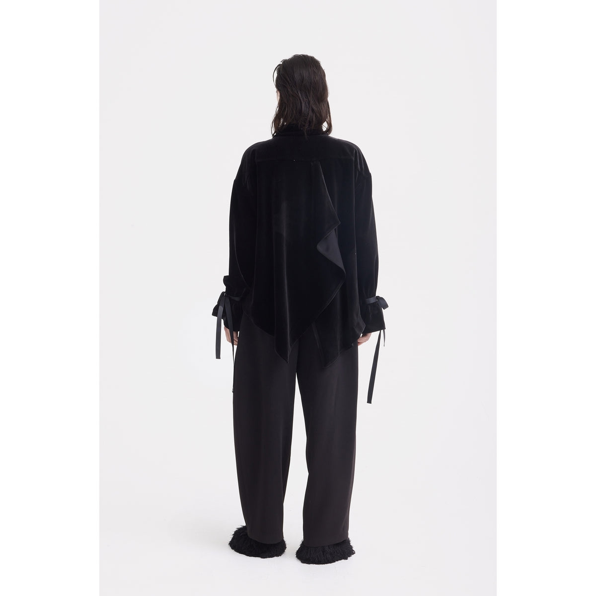 A person with medium-length dark hair faces away, wearing the JULIA ALLERT Evening Velvet Wrap Jacket With Silk Lining in black and wide-leg textured-hem pants, standing against a plain white background.