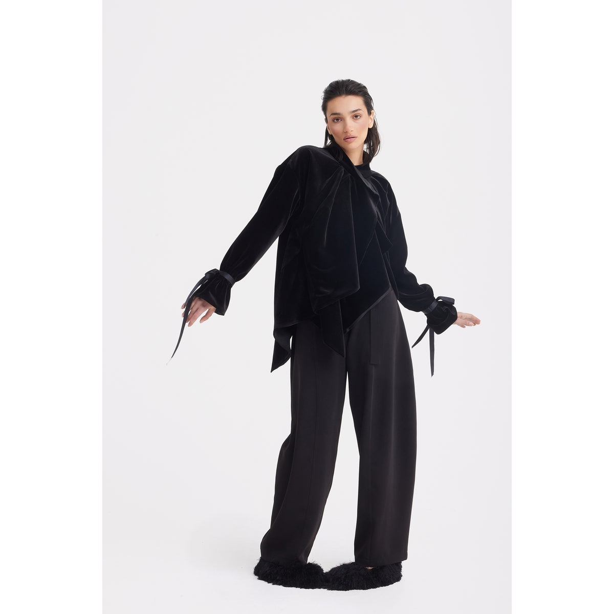 A woman, standing confidently against a white background, wears the JULIA ALLERT Evening Velvet Wrap Jacket With Silk Lining in black, featuring ribbon-detailed cuffs, paired with wide-leg black pants.