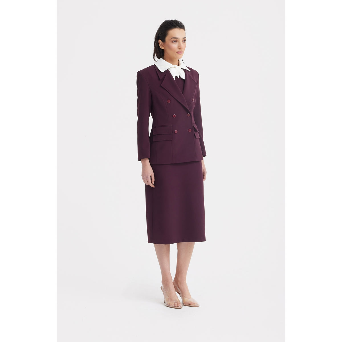 A woman wears the JULIA ALLERT Classic Tailored Double-Breasted Blazer in burgundy with a matching midi skirt, a white collared shirt with a large bow, nude heels, and straight dark hair against a plain white background.