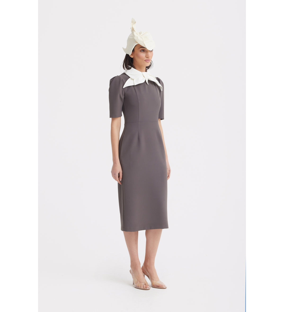 A woman poses against a plain background in the JULIA ALLERT Elegant Midi Dress With Contrast Bow Collar - Taupe, featuring a fitted taupe silhouette, short sleeves, and a striking contrast bow collar.