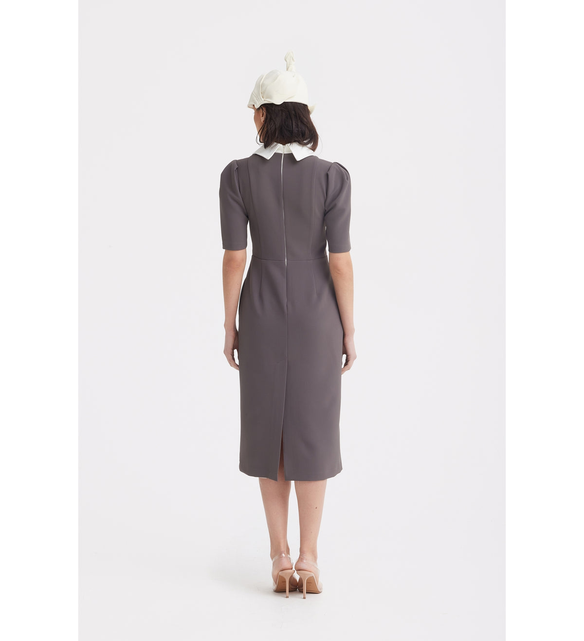A person faces away, wearing the JULIA ALLERT Elegant Midi Dress With Contrast Bow Collar - Taupe, paired with beige heels and a white hat against a plain white background.