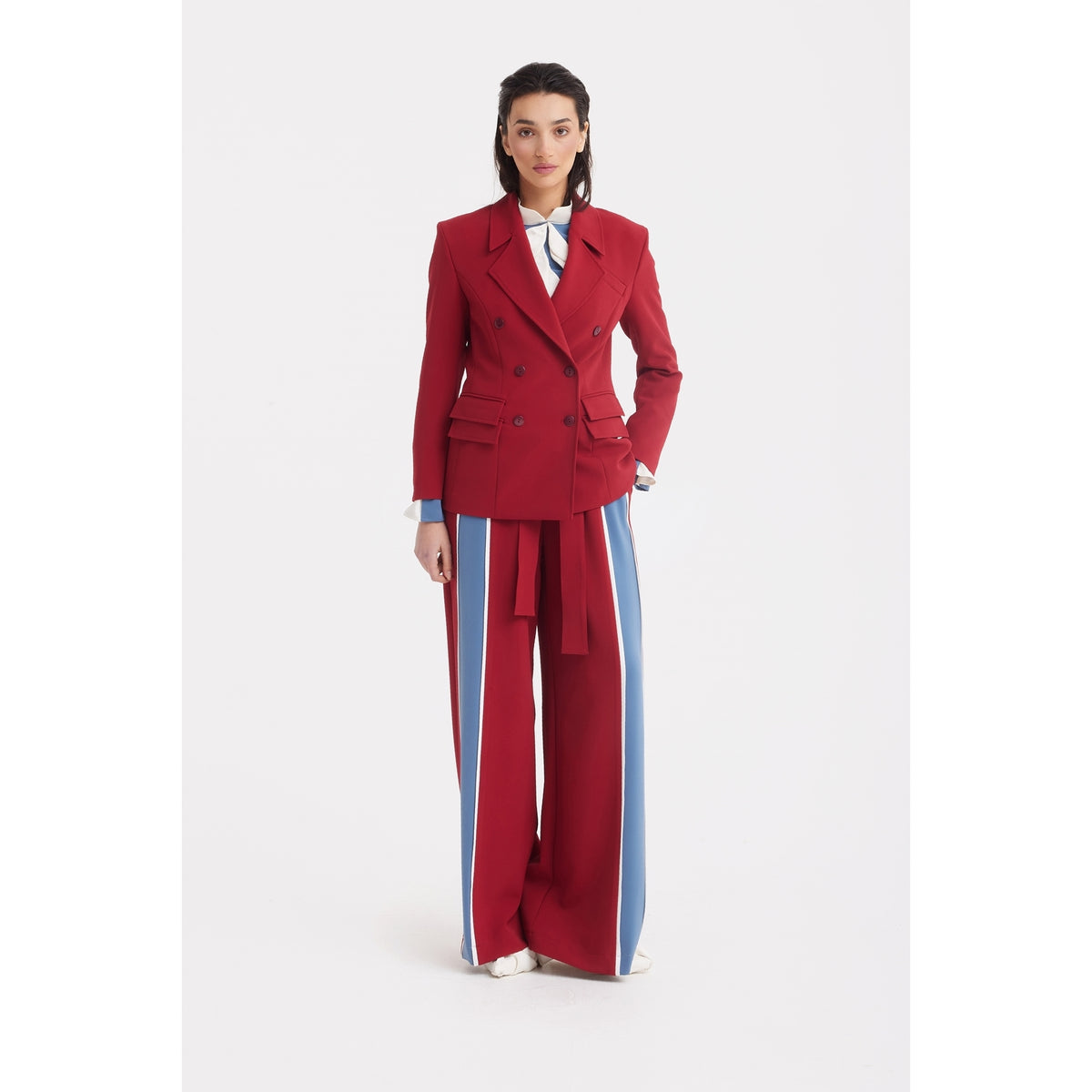 A woman stands against a white background wearing a red double-breasted blazer and JULIA ALLERT Belted High Waist Wide Leg Pants in Burgundy, paired with a white shirt and white shoes.