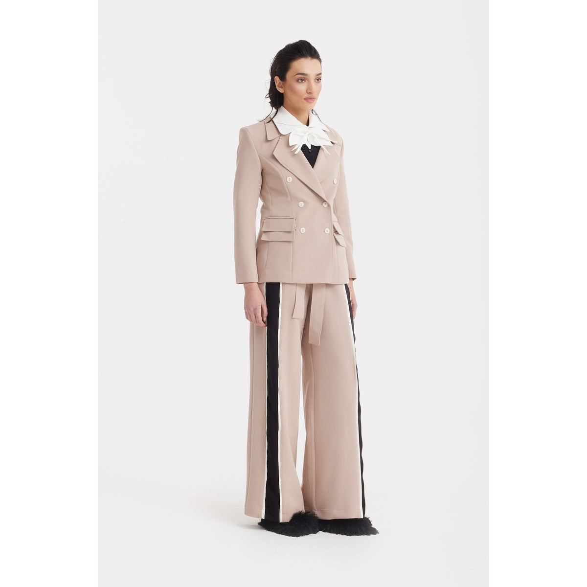 A woman poses against a white backdrop wearing the JULIA ALLERT Classic Tailored Double-Breasted Blazer in beige with a white collar, paired with matching wide-leg pants featuring black side stripes and black shoes.