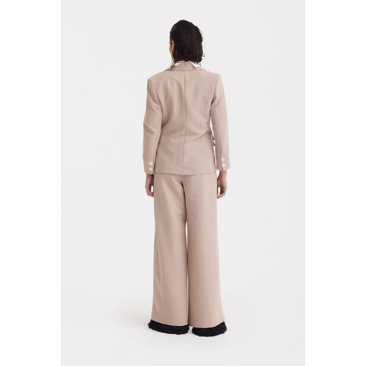 A person faces away, wearing the JULIA ALLERT Classic Tailored Double-Breasted Blazer in beige with wide-leg pants featuring black fringe at the hem, long sleeves, and white cuff buttons. The background is plain white.