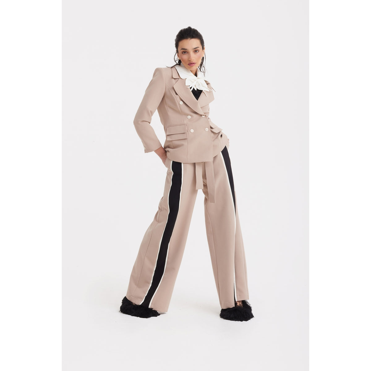A woman models the JULIA ALLERT Classic Tailored Double-Breasted Blazer in beige, paired with matching wide-leg pants featuring black side stripes and feathered cuffs, completed with a bow at the collar.
