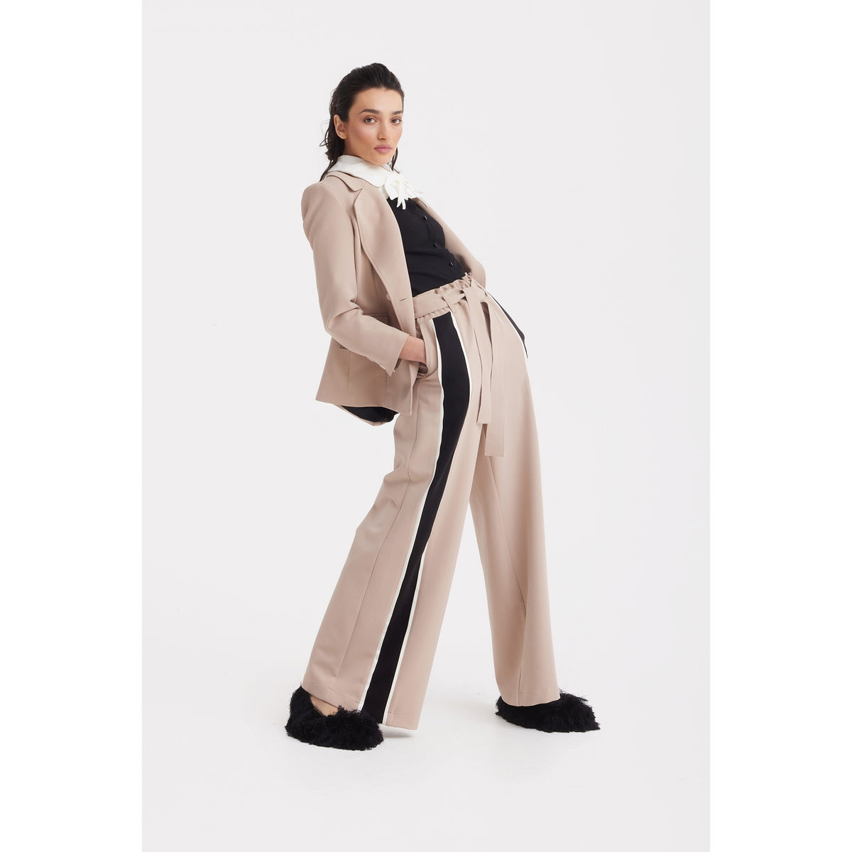 A woman poses in the JULIA ALLERT Classic Tailored Double-Breasted Blazer in beige, styled with matching wide-leg pants with a black side stripe, a black top featuring a white collar, and black furry shoes against a plain white background.