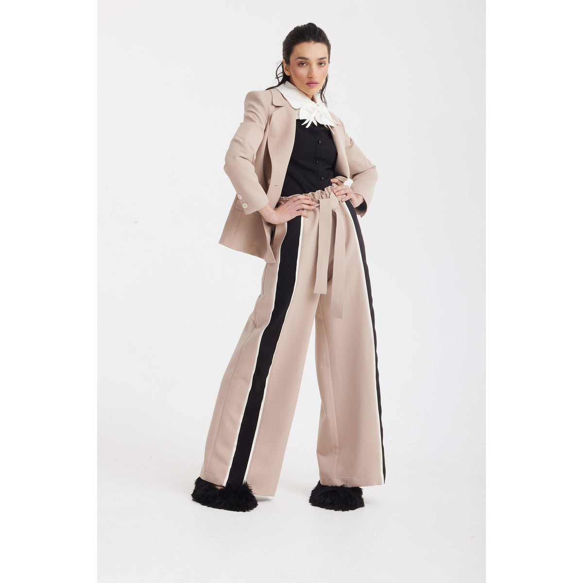 A woman poses confidently in the JULIA ALLERT Classic Tailored Double-Breasted Blazer in beige with wide-leg pants featuring black side stripes, a matching belt, a black shirt with white collar, and black furry shoes against a plain white background.