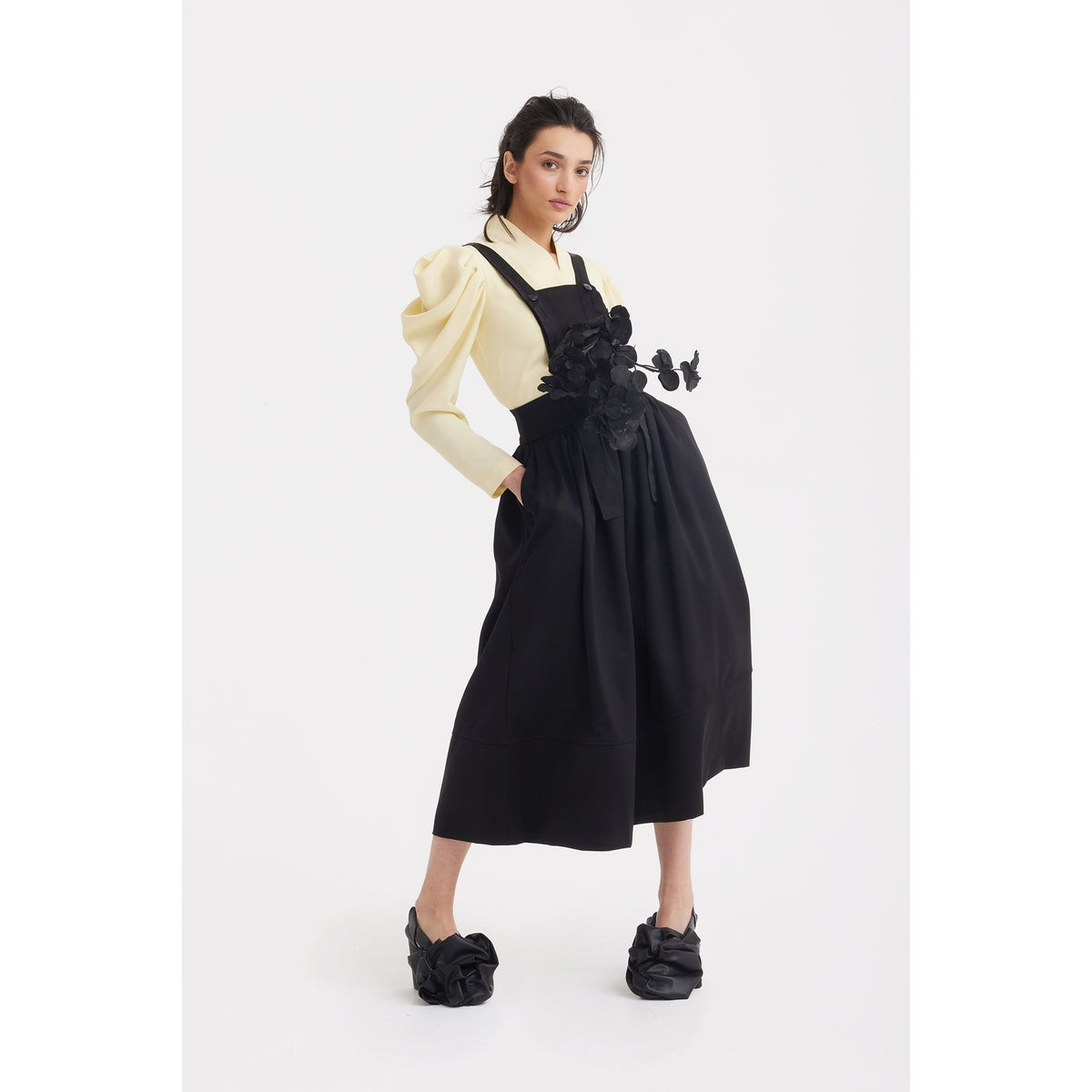 Model in a JULIA ALLERT Sculpted V-Neck Blouse with Dramatic Sleeves in pale yellow and a black pinafore dress with floral appliqué, posing against a white background.