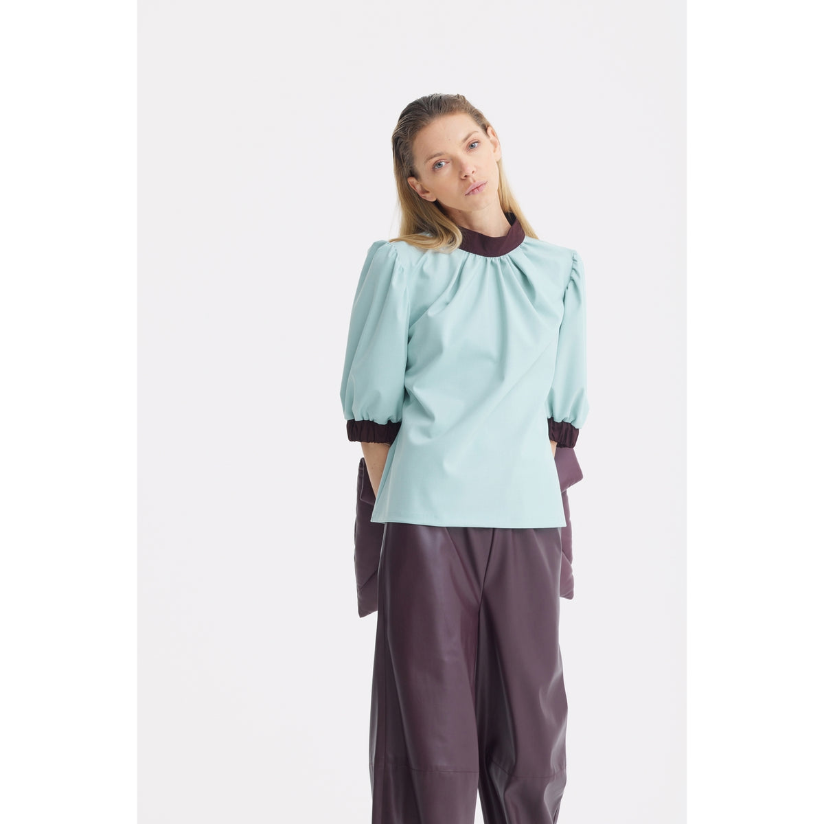 A person with long blonde hair wears a JULIA ALLERT Textured Short Sleeve Blouse in light blue, paired with loose burgundy pants, standing against a plain white background.