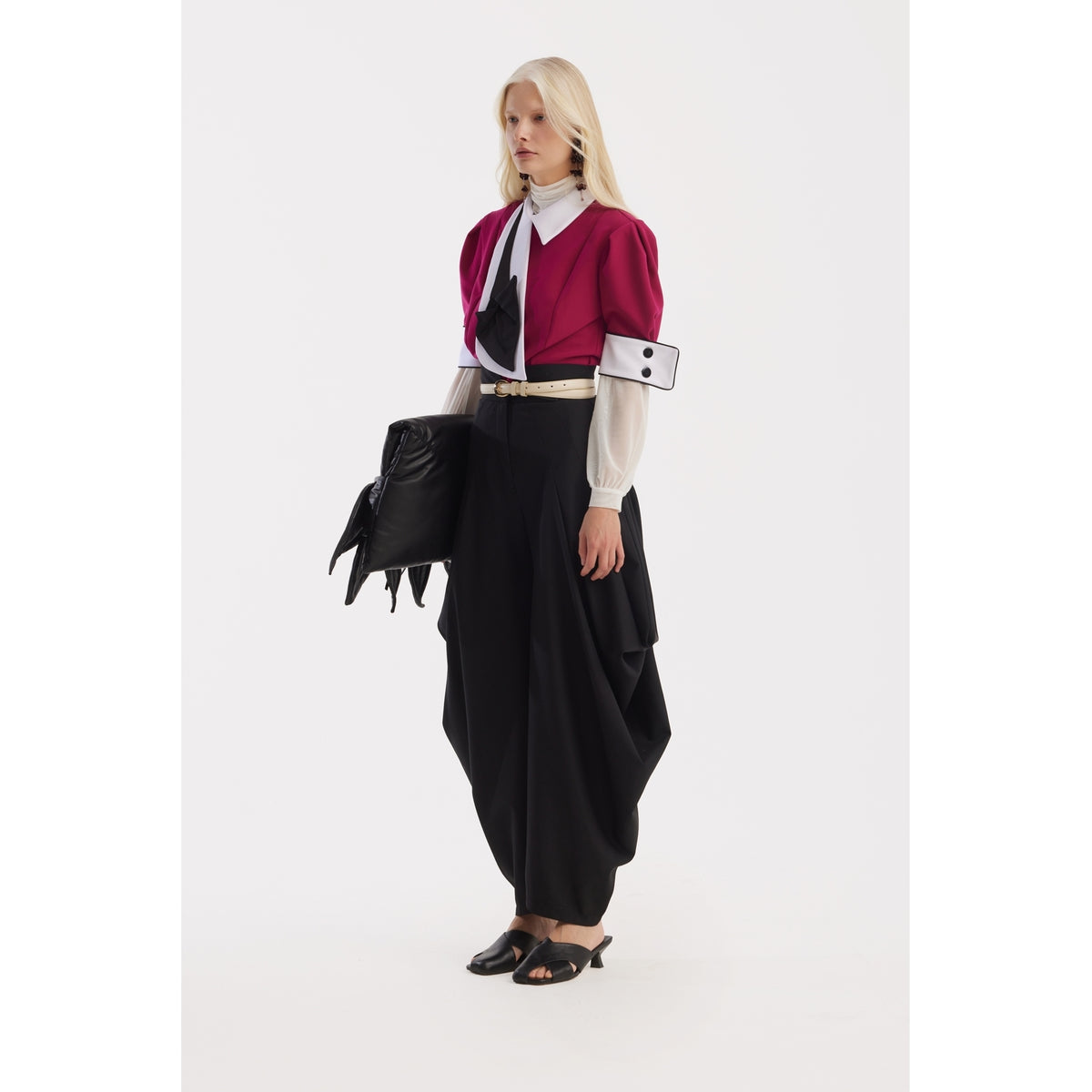 A model with long blond hair wears the JULIA ALLERT Statement Blouse With White Collar And Cuffs in fuchsia, paired with loose black trousers and a sculptural bag, standing against a white background.