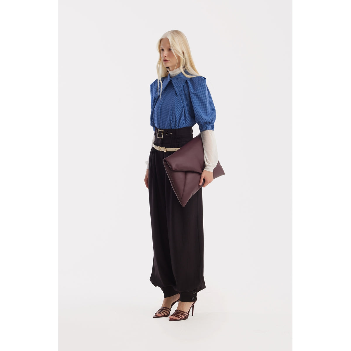 A woman with long blonde hair wears the JULIA ALLERT Designer Plaid Puff Sleeve Blouse in blue over a white top, paired with wide black pants, heeled sandals, and a large brown clutch. She stands against a plain white background.