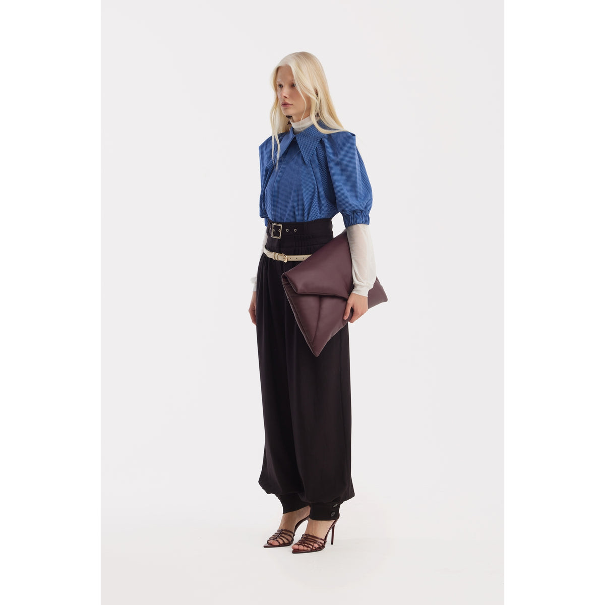 A woman with long blonde hair wears JULIA ALLERT Belted High-Waist Balloon-Leg Pants in black, styled with a blue blouse over a white turtleneck, brown heeled sandals, and a large brown clutch against a plain white background.