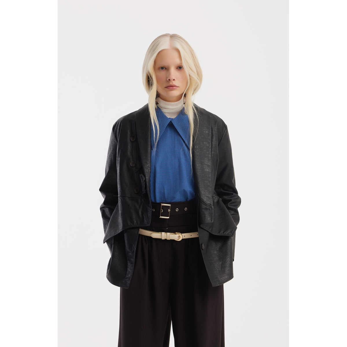 A person with long blonde hair wears a JULIA ALLERT black leather jacket, Designer Plaid Puff Sleeve Blouse - Blue, white turtleneck, and high-waisted brown pants with a beige belt, standing against a plain white background.