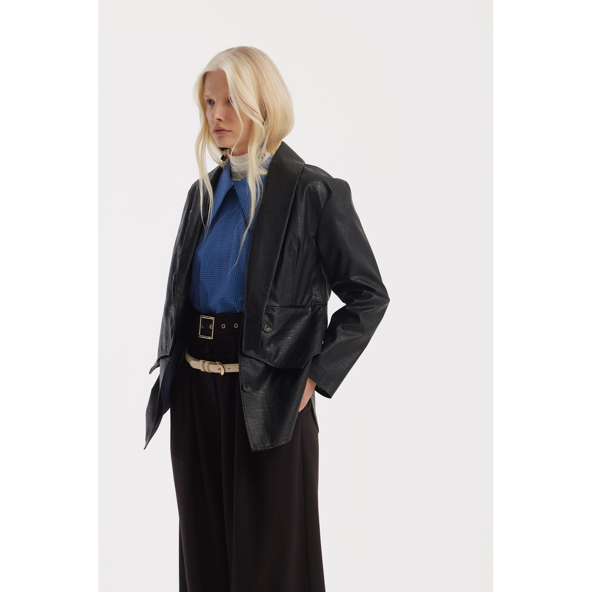 A person with long blonde hair wears a black leather blazer over the JULIA ALLERT Designer Plaid Puff Sleeve Blouse in blue, paired with wide-leg black trousers and two belts, standing against a plain white background.