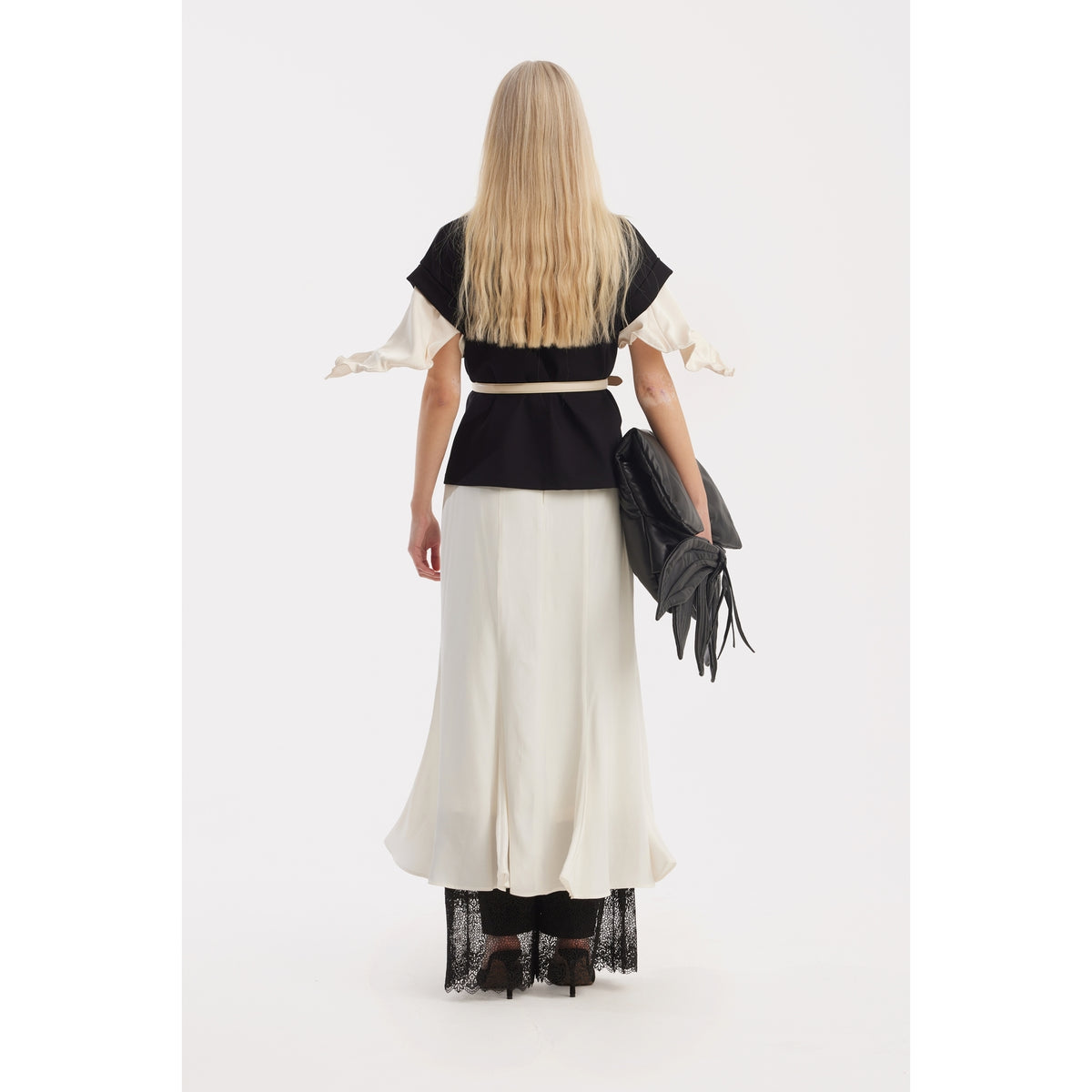 A person with long blonde hair stands facing away, wearing the JULIA ALLERT Crew-Neck Jersey T-Shirt With Flower in black, paired with a long skirt and flared sleeves. They hold a large black clutch and wear black shoes against a plain white background.