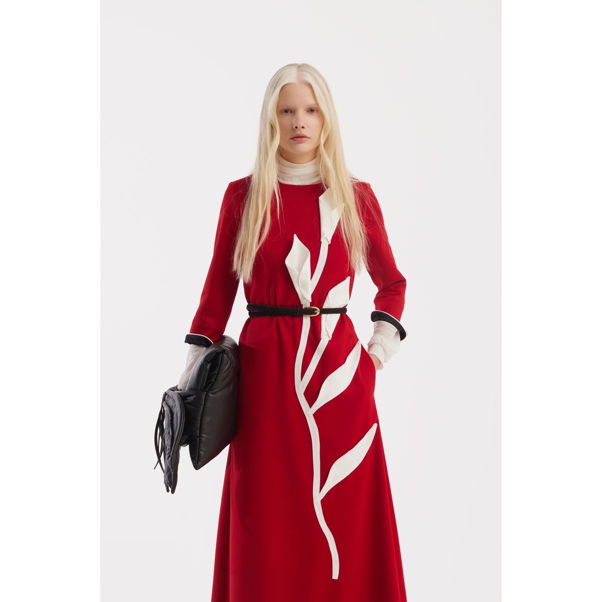 A woman with long blonde hair wears the JULIA ALLERT Art-Inspired Semi-Fitted Three-Quarter Sleeves Dress in red, styled with a black belt and clutch, standing against a plain white background.