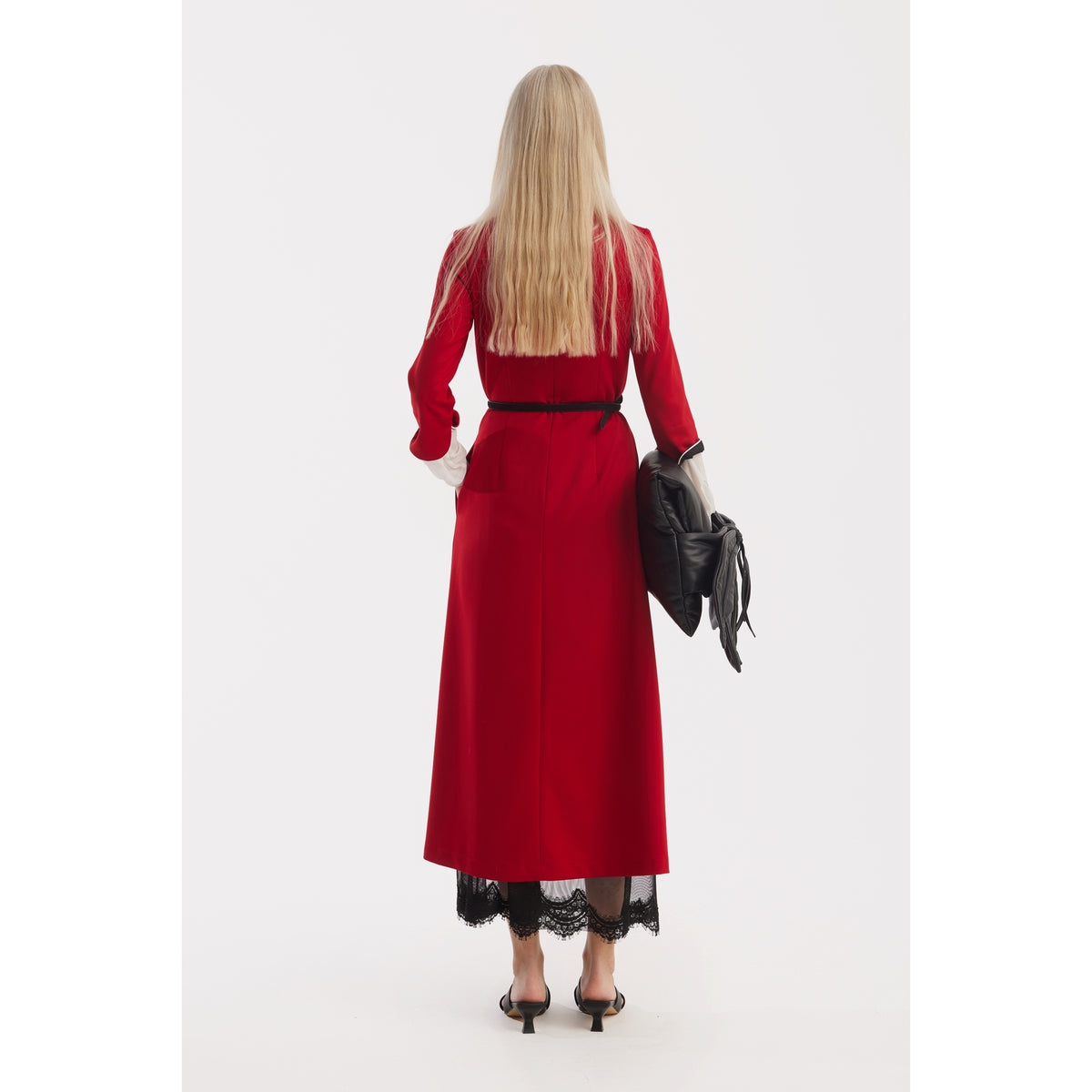 A woman with long blonde hair stands facing away against a white background, wearing JULIA ALLERT's Art-Inspired Semi-Fitted Three-Quarter Sleeves Dress in red, paired with black heels and holding a black jacket in her right hand.