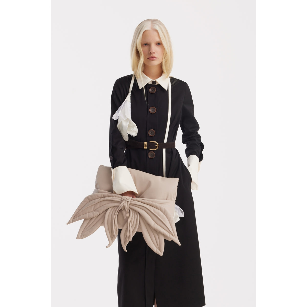 A woman with long blonde hair wears the Monochrome Midi Shirt Dress - Black &amp; White by JULIA ALLERT, styled with large buttons, a white collar and cuffs, and a black belt. She holds a beige leaf-shaped oversized clutch against a plain white background.