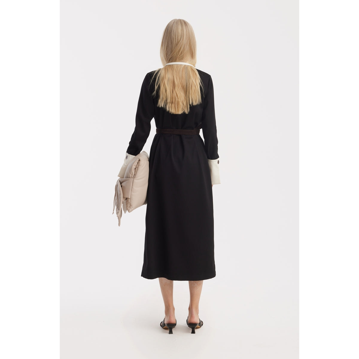 A woman with long blonde hair faces away, wearing the JULIA ALLERT Monochrome Midi Shirt Dress - Black &amp; White with light cuffs and heels, holding a light handbag by her side against a plain white background.