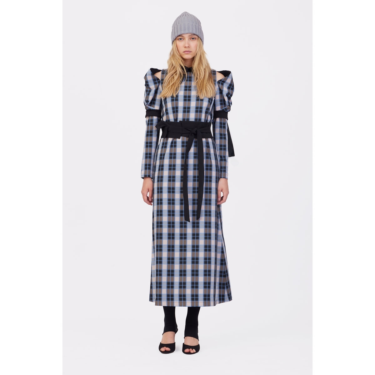 A woman faces forward wearing the JULIA ALLERT Stylish Cold Shoulder Long Sleeve Dress With Belt Blue Check, paired with black open-toe heels, black leggings, and a gray knit beanie against a plain white background.