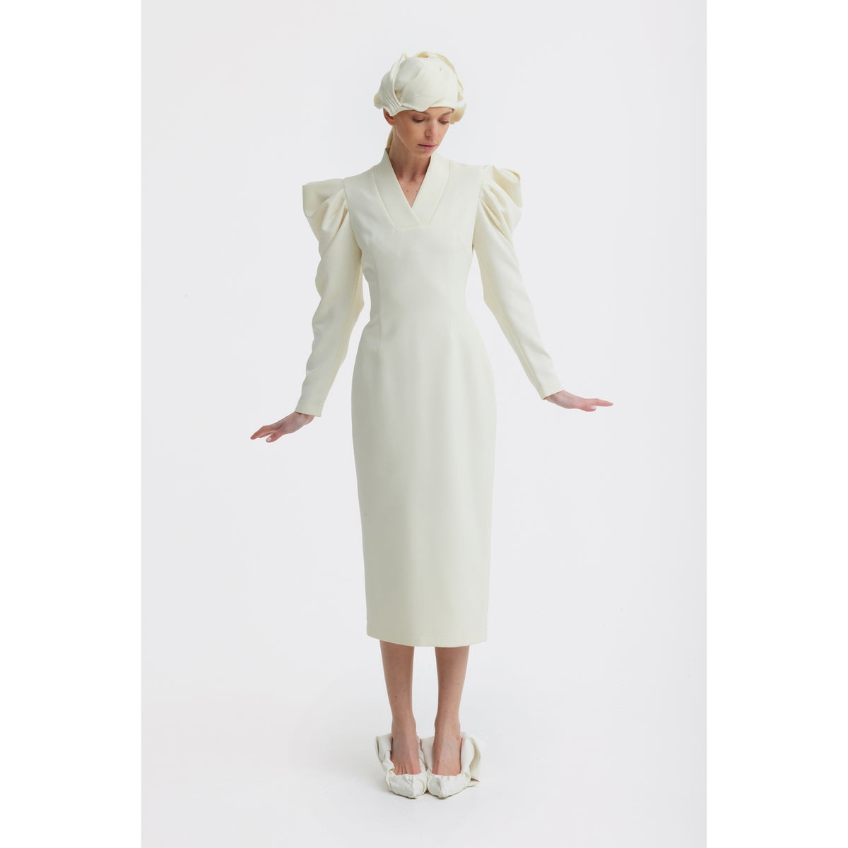 Against a white background, a person wears the JULIA ALLERT Crepe Midi Dress With Statement Sleeves in ivory, paired with a matching cap and pointed shoes, their arms gently extended down by their sides.