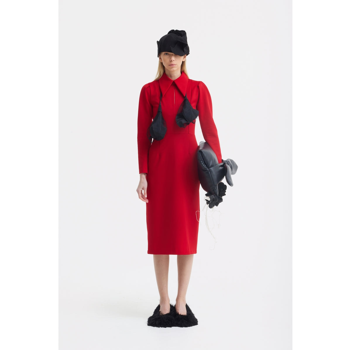 A woman wears the JULIA ALLERT Solid Formal Midi Dress in red, paired with black fuzzy slippers and a dramatic hat with a fabric veil. She accessorizes with a sculptural neckpiece and holds a balloon-like object against a white backdrop.