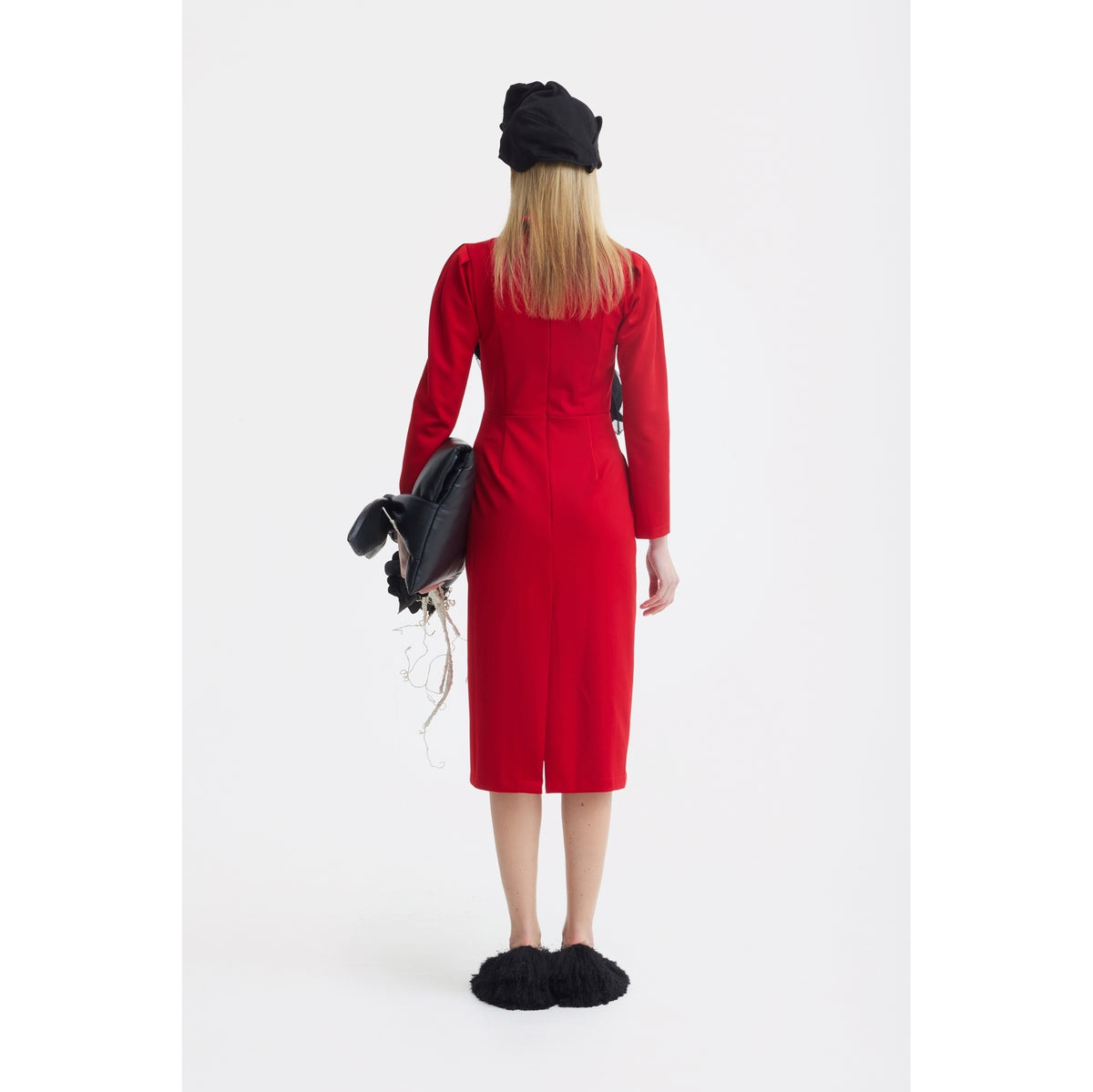 A woman faces away, wearing a JULIA ALLERT Solid Formal Midi Dress - Red, black slippers, and a black hat. She holds a black jacket over her left arm against a plain white background.