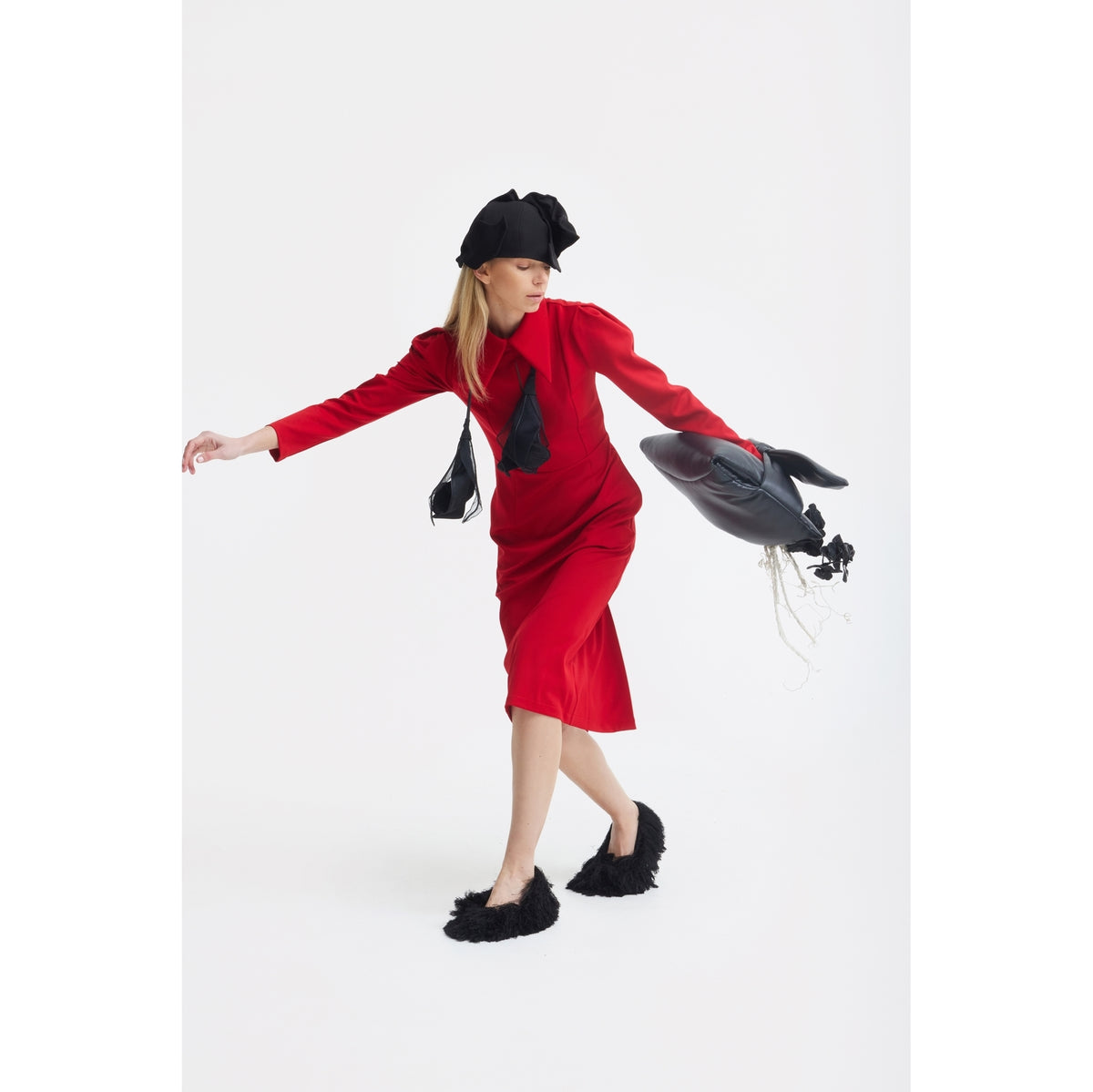 A woman poses on one foot in a JULIA ALLERT Solid Formal Midi Dress - Red, with black furry slippers, a black hat, and a fish-shaped black bag against a plain white background.