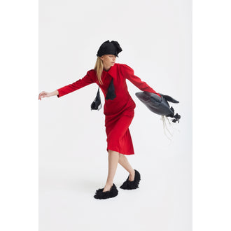 A woman poses on one foot in a JULIA ALLERT Solid Formal Midi Dress - Red, with black furry slippers, a black hat, and a fish-shaped black bag against a plain white background.