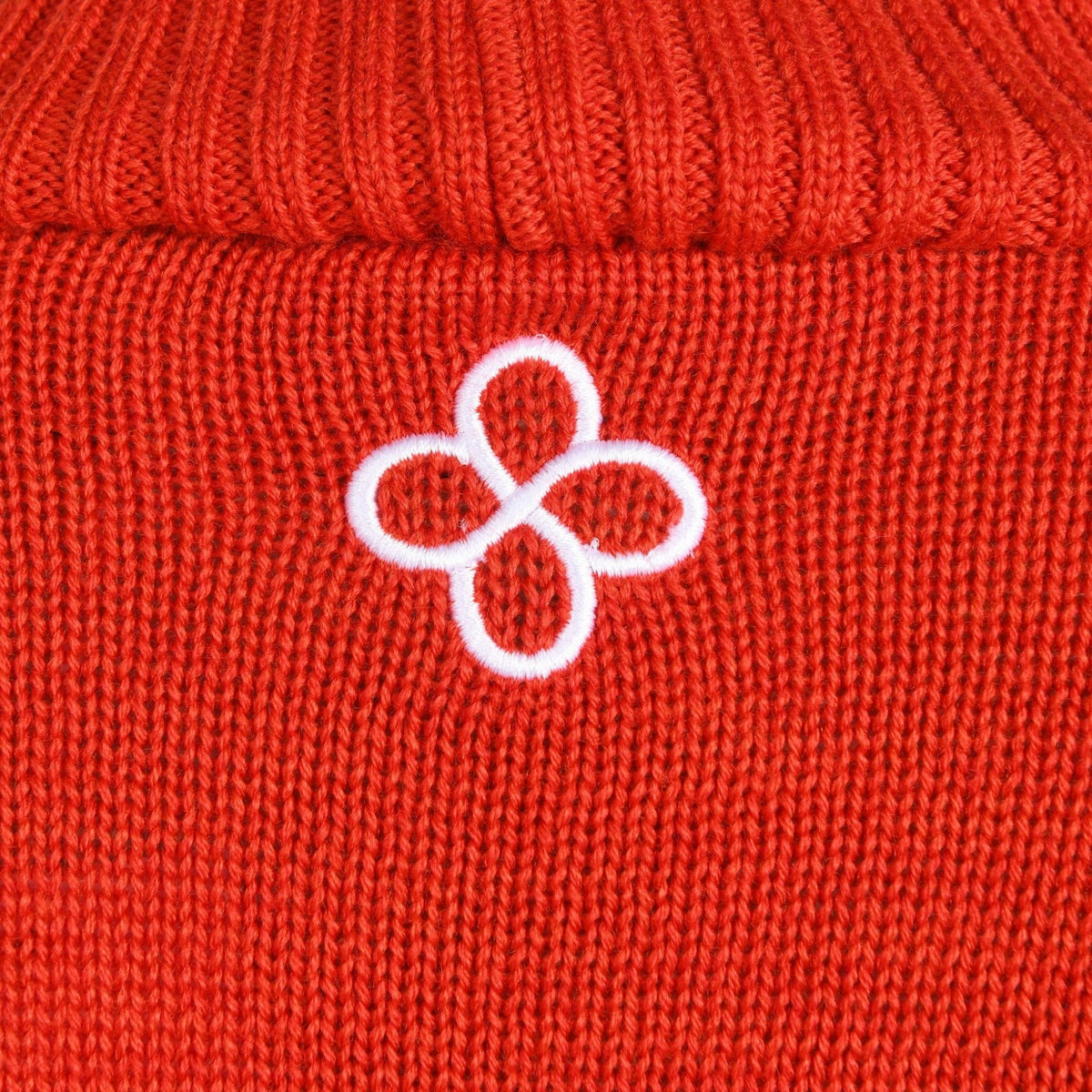 Close-up of a red knitted fabric with a white embroidered logo.