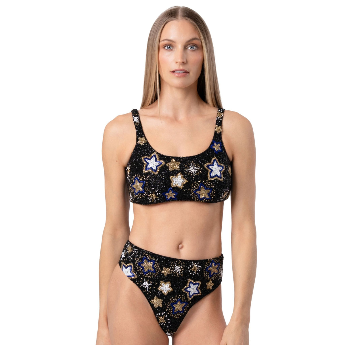A woman with straight, light brown hair models the SELF-ADORE Celeste Hand-Beaded Embellished Bikini Top in black, featuring colorful star patterns, while standing against a plain white background.
