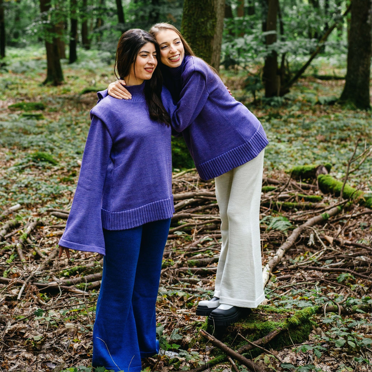 Two women in purple sweaters hugging in a forest setting