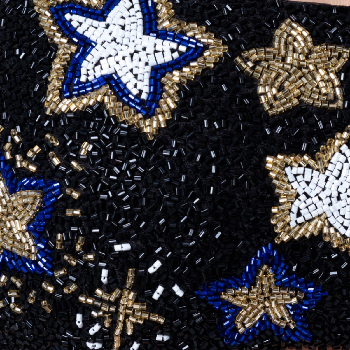 Close-up of the SELF-ADORE Celeste Hand-Beaded Embellished Bikini Bottom in black, featuring intricate white, blue, and gold star patterns crafted with small cylindrical beads for a stunning swimwear look.