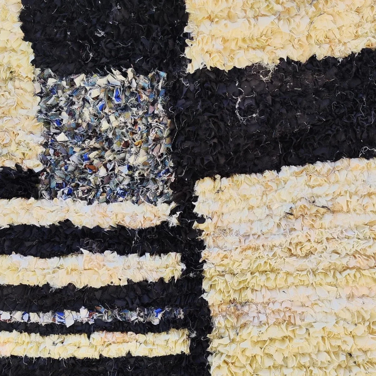 Close-up of a textured rug with black, beige, and multicolored pattern