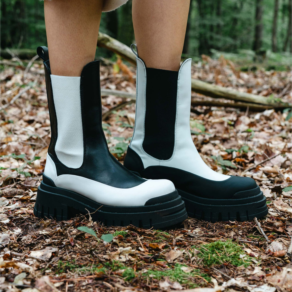 Black and white boots on a person standing in a forest setting