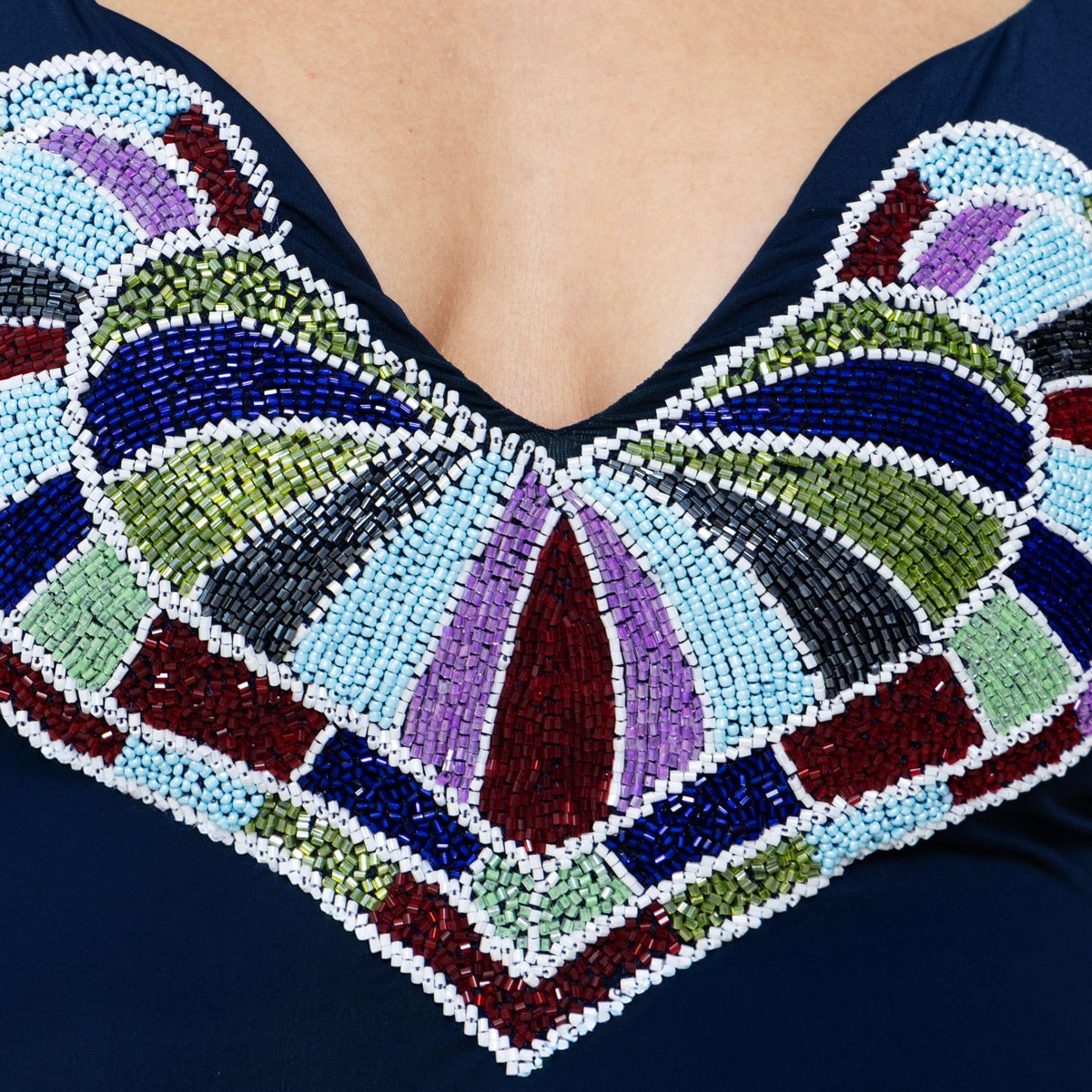 A close-up of a person's upper chest wearing the SELF-ADORE Amor Hand-Beaded Embellished One-Piece Swimsuit in Navy, featuring intricate, colorful geometric beadwork reminiscent of a hand-beaded heart motif.