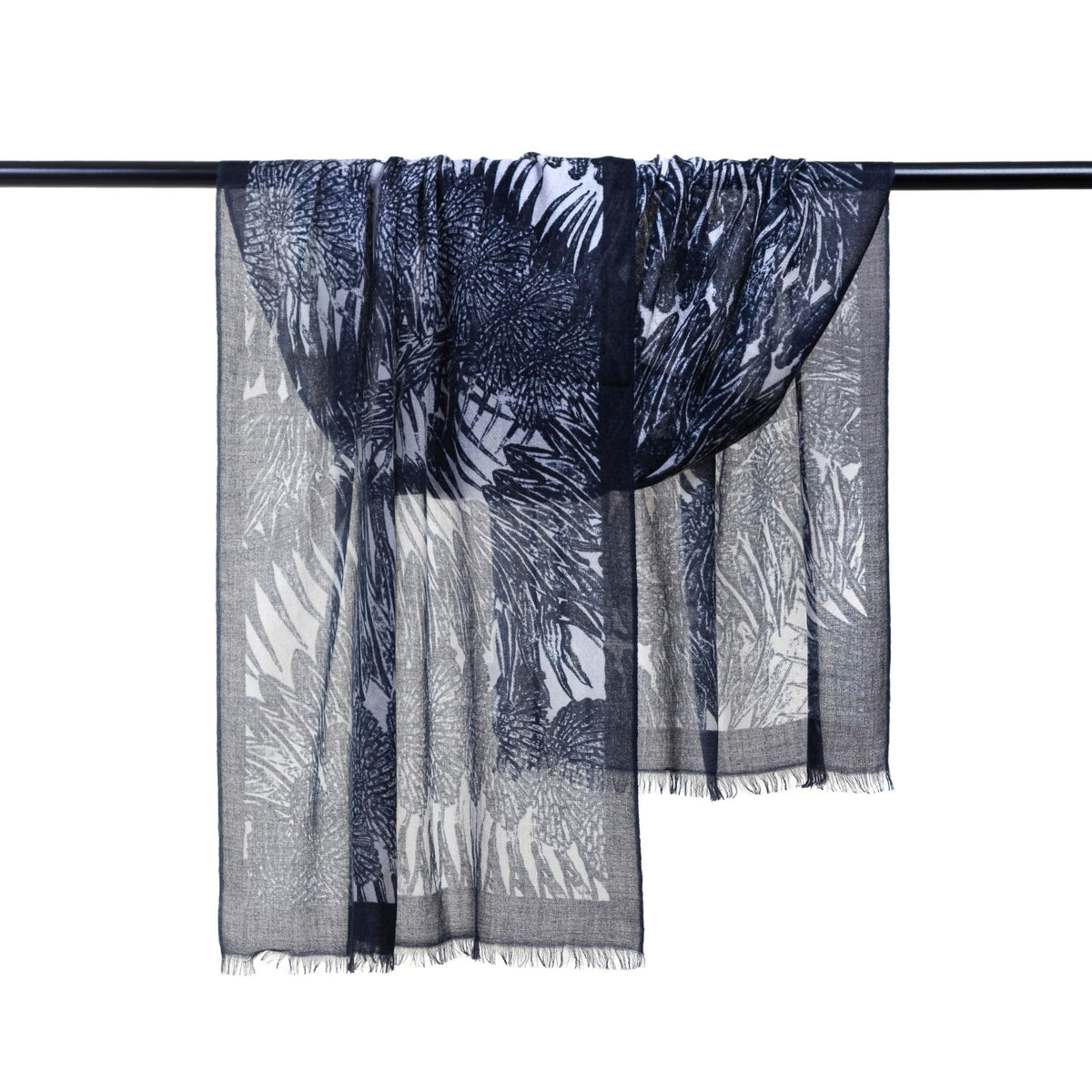 The Black Ella Monochrome Stole by OO-TO is a lightweight, semi-sheer cashmere scarf handcrafted in Nepal. Draped over a black rod, it features delicate fringe and an elegant mix of monochrome leaf and floral patterns.