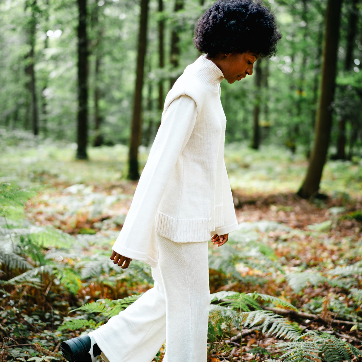 Person in a white outfit walking through a forest