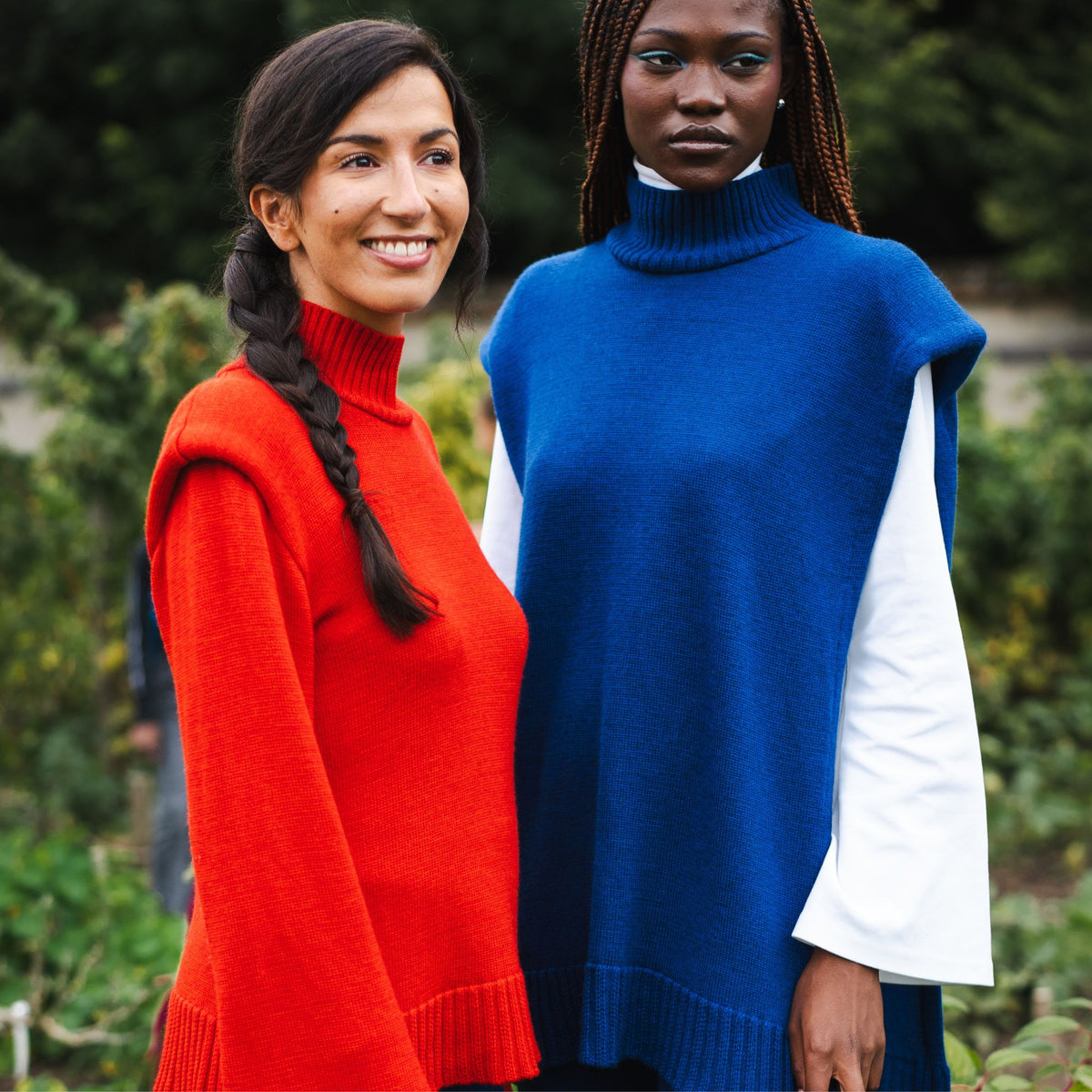Two women wearing colorful sweaters standing outdoors with a blurred green background