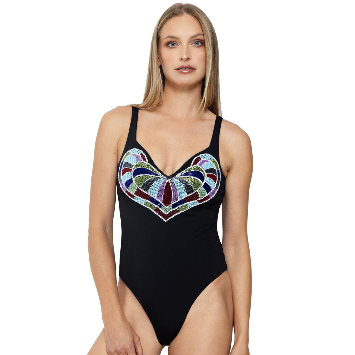 A woman with long straight hair models the SELF-ADORE Amor Hand-Beaded Embellished One-Piece Swimsuit in black, showcasing a colorful geometric heart-shaped pattern on the chest. She stands facing forward against a plain white background.