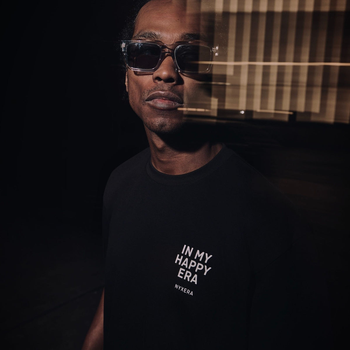Person wearing sunglasses and a black t-shirt with text in a dark setting