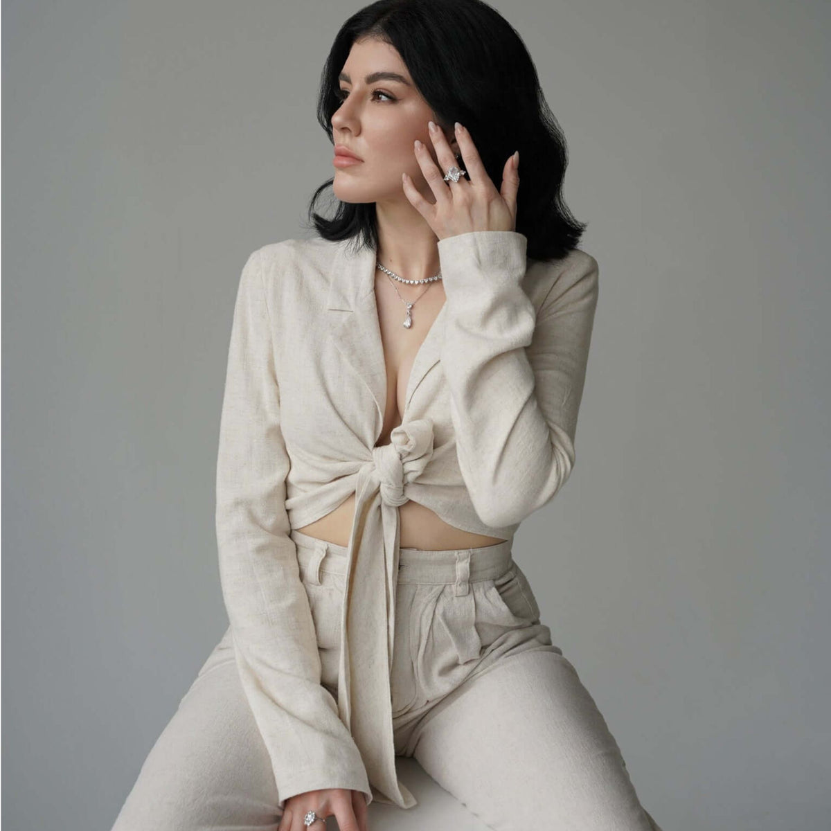 Woman wearing a stylish beige outfit with a tied front top against a gray background