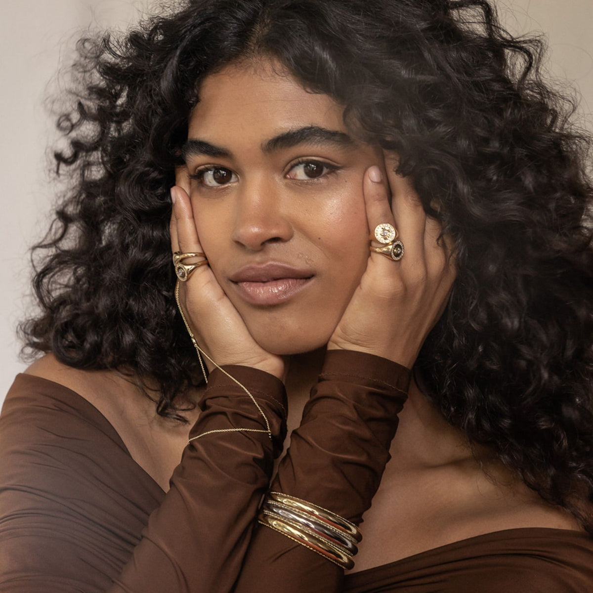 Woman with curly hair wearing gold jewelry against a neutral background