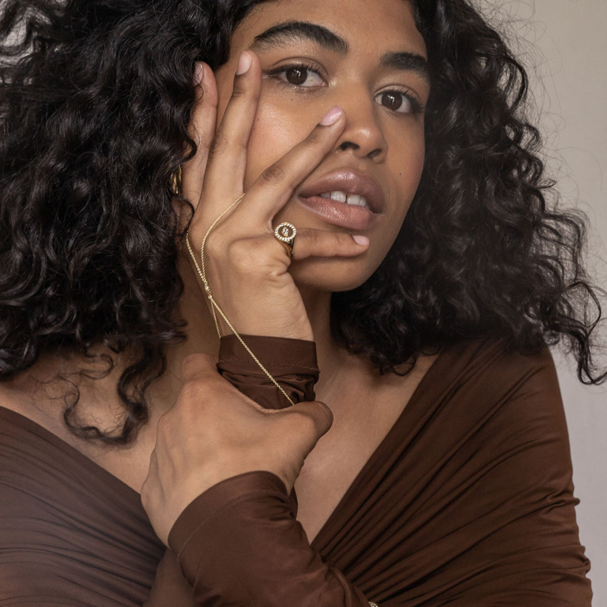 Woman with curly hair wearing a brown top against a neutral background