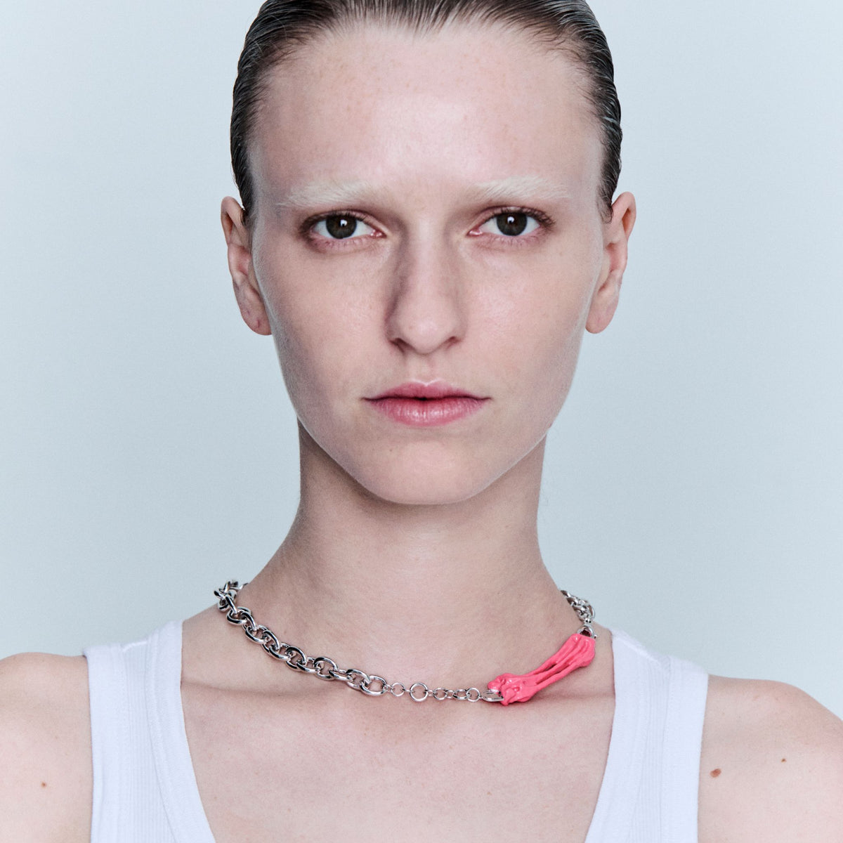 Person wearing a chain necklace with a pink accent on a light gray background